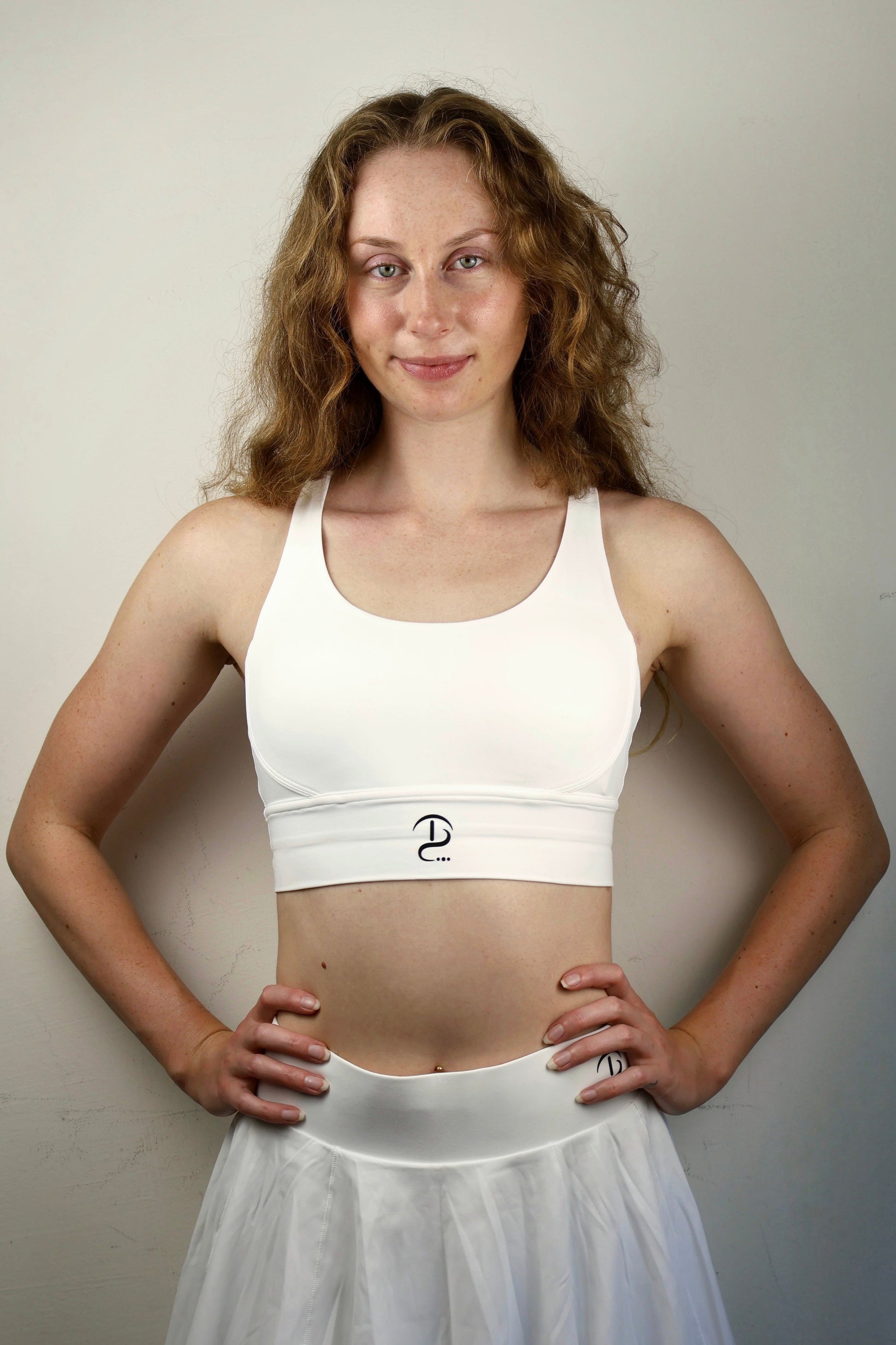 Woman wearing a white sports bra and skirt against a plain background