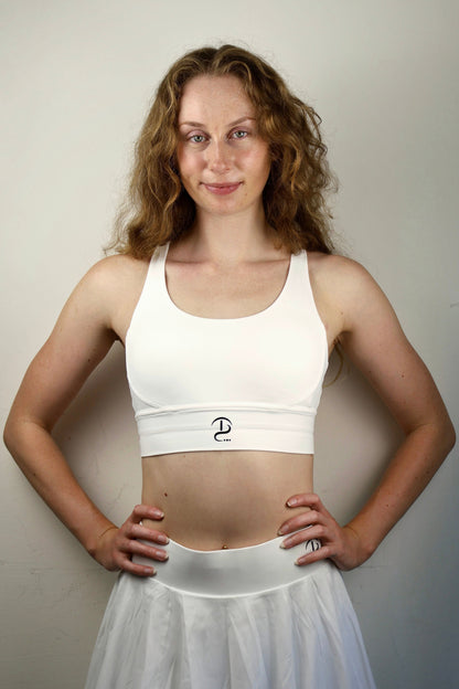 Woman wearing a white sports bra and skirt against a plain background